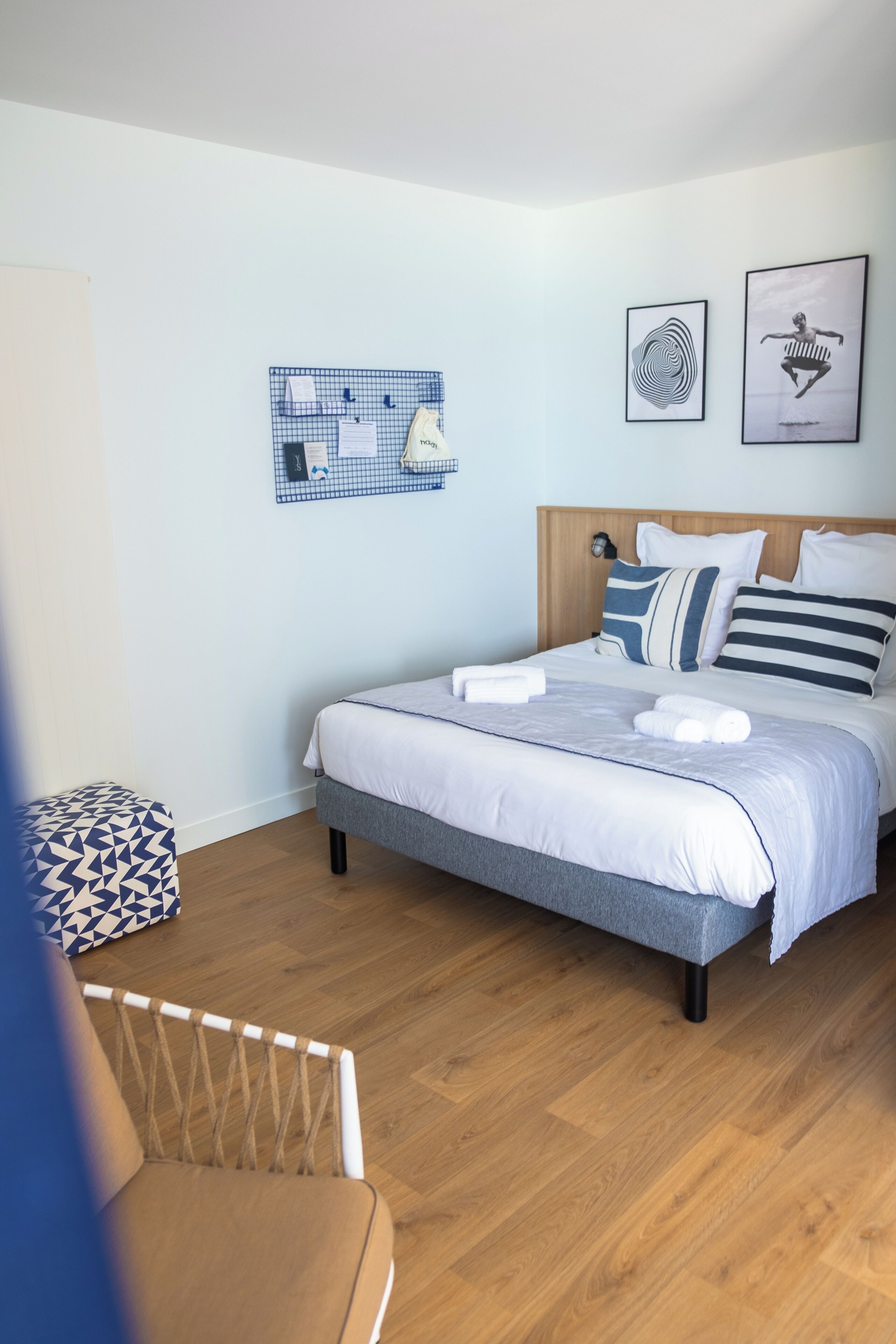 A neatly arranged bedroom with a bed, a small seating area, and a wall-mounted board with items.