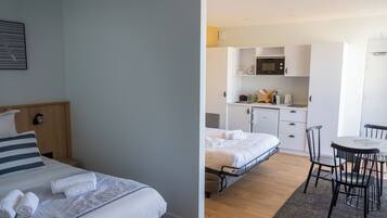 Ein Zimmer mit zwei Betten, einem Esstisch mit Stühlen, einer Küchenzeile inklusive Mikrowelle und einem kleinen Schrank.