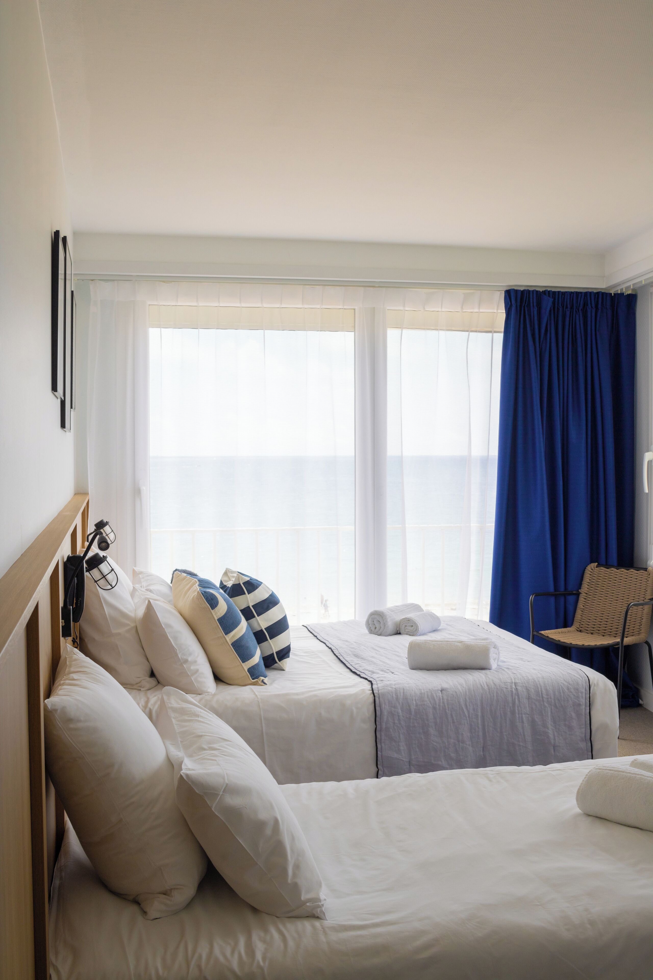 Ett hotellrum med två sängar, en stol och ett stort fönster med gardiner.