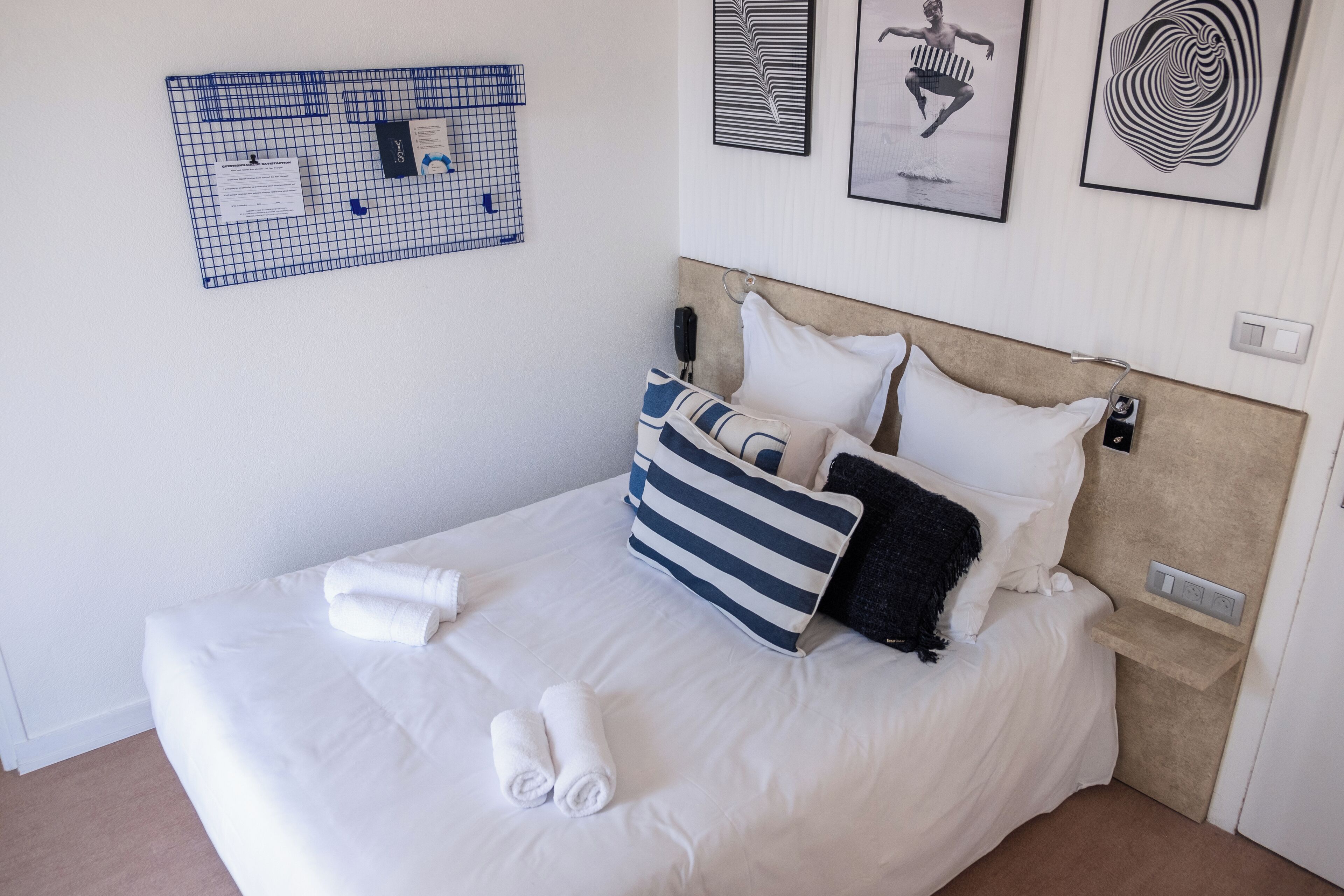 A neatly made bed with white linens, striped pillows, and rolled towels.