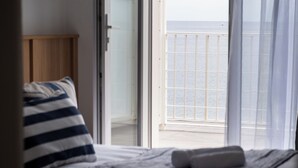 Une chambre à coucher avec un lit, un coussin à rayures et une vue sur la mer, visible à travers la porte d’un balcon.