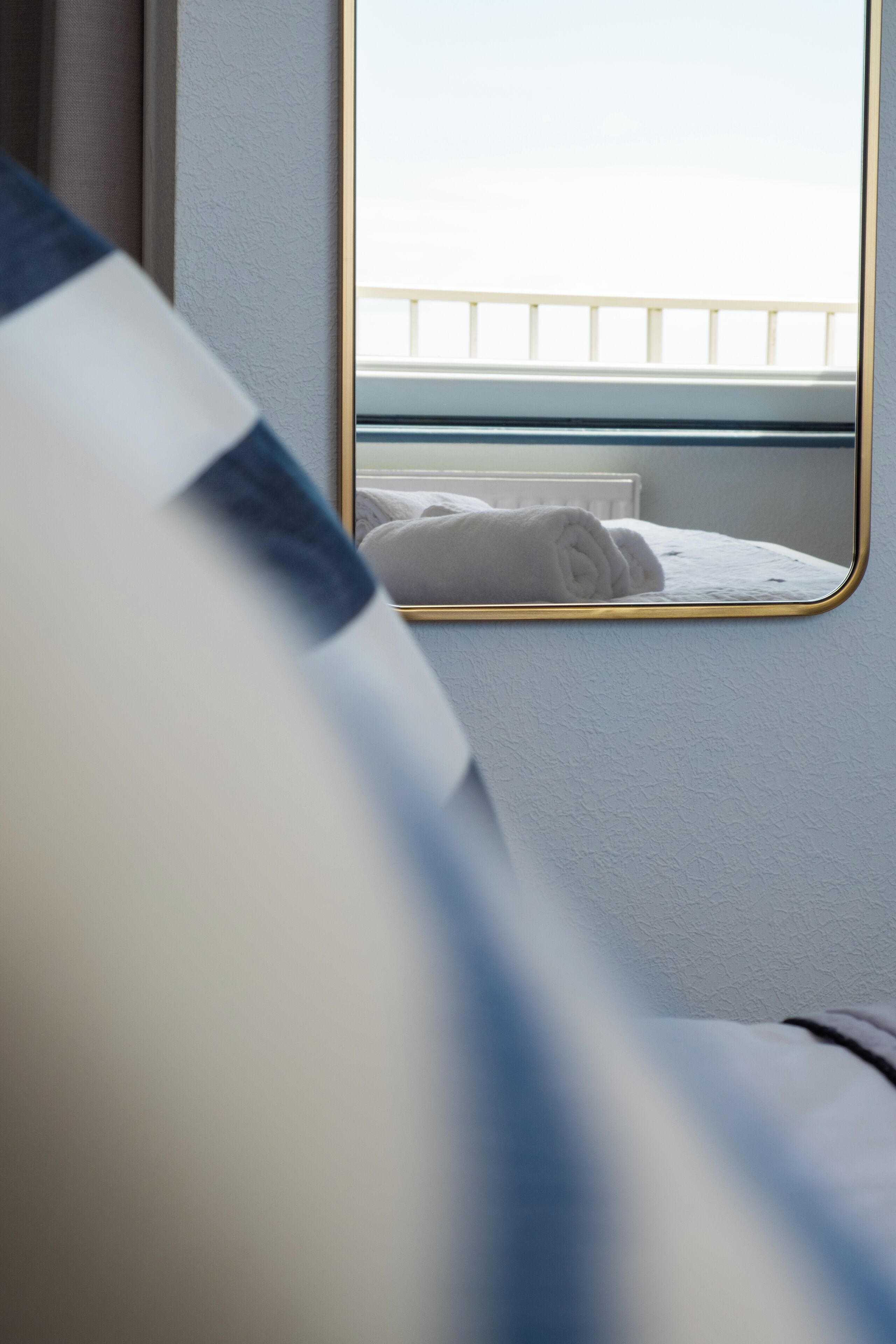 A hotel room with a bed, a window with a view of a balcony, and a mirror reflecting the room.