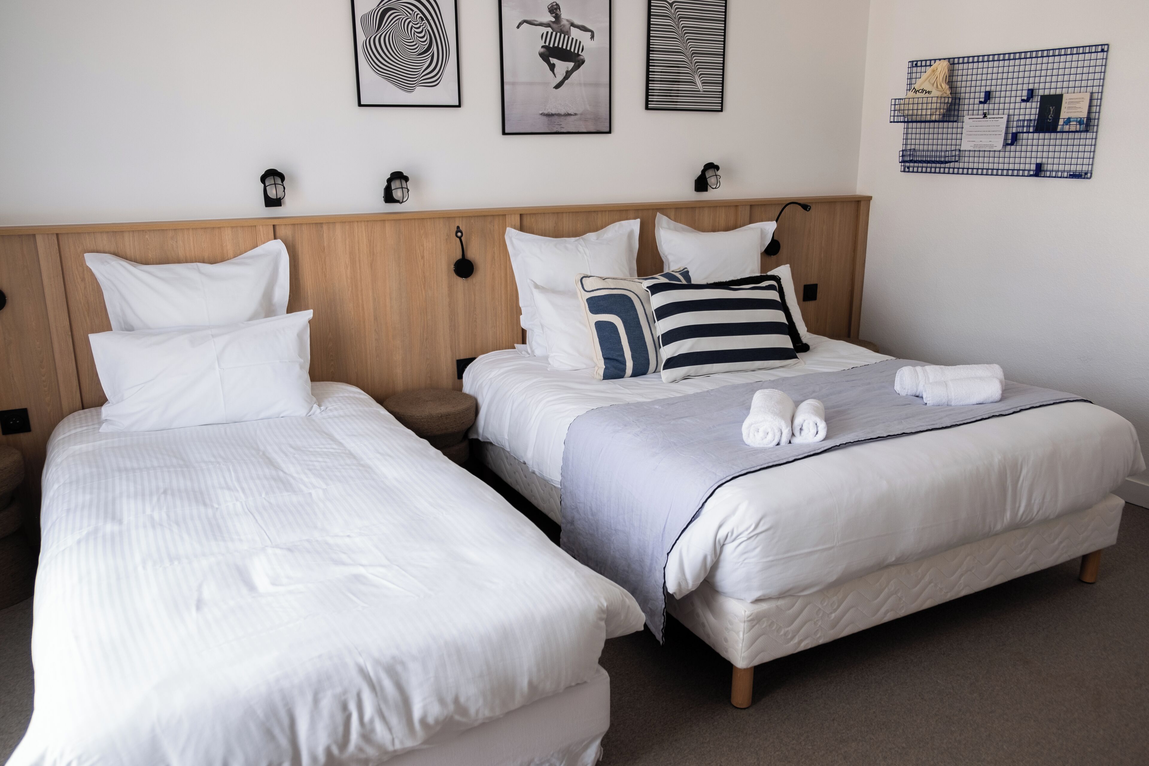 A hotel room with two single beds, a wooden headboard, white bedding, and a wall-mounted bulletin board with notes and pictures.