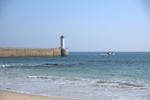 A lighthouse by the sea, a concrete barrier, and a boat in the distance.