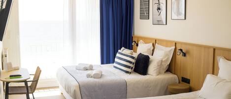 A hotel room with two beds, a desk, and a chair. There are towels on the beds and a window with curtains.
