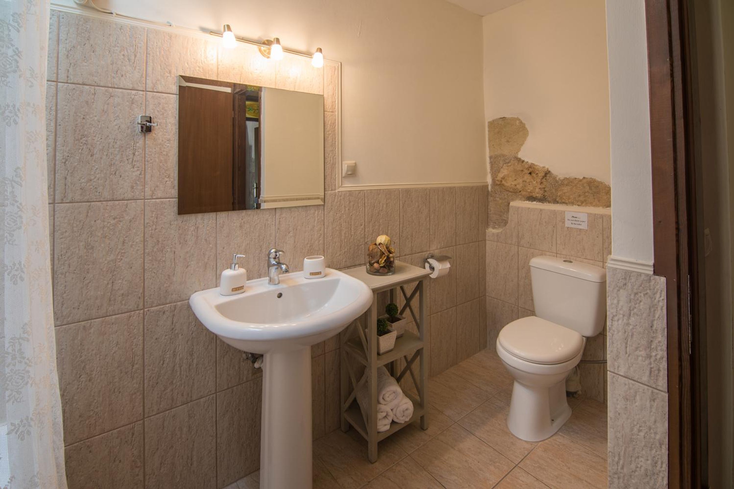 A bathroom with a sink, mirror, toilet, and a shelf with towels.
