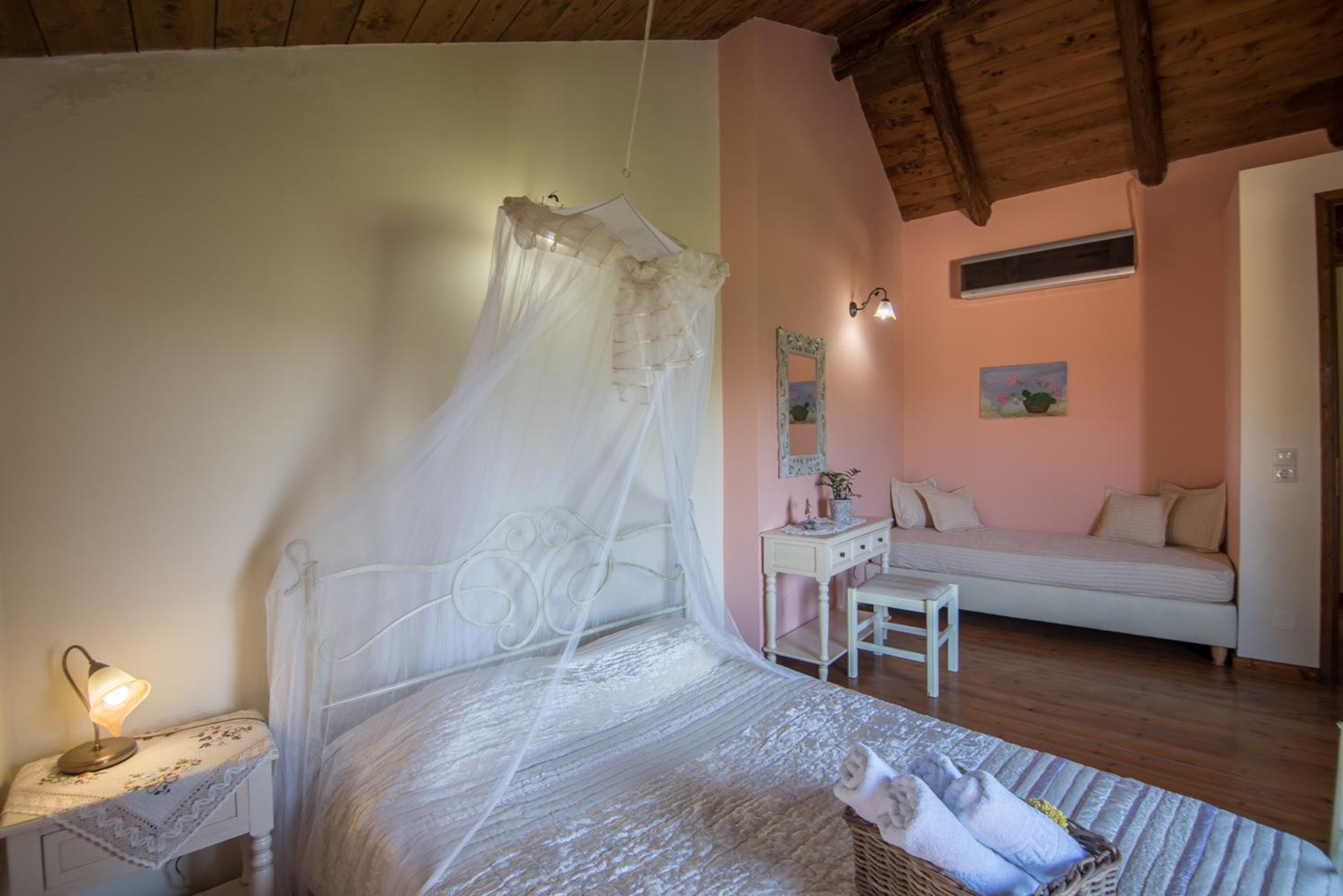 Une chambre à coucher avec un lit à baldaquin, une table de chevet avec une lampe, une petite chaise, un canapé et un miroir fixé au mur.