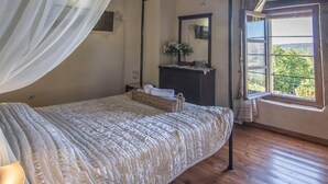 A bedroom with a wooden ceiling, a bed with a white canopy, a dresser, a mirror, and a window with a view. - Villa Kourkoulios in Apokoronos (Apokoronas)