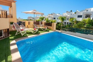 A swimming pool with lounge chairs and an umbrella, surrounded by greenery and modern buildings. - Casa Eva in Nerja With 3 Bedrooms and 3 Bathrooms (Nerja)