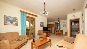 A living room with a sofa, coffee table, and a television. There is a kitchen area with a dining table and chairs. - Villa Vaso in Roussospiti (Rethymno)