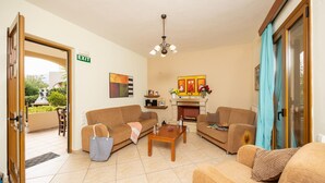A living room with two sofas, a coffee table, and a fireplace. There is a door labeled "EXIT" and a window with curtains. - Villa Vaso in Roussospiti (Rethymno)