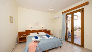 A bedroom with a bed, bedside tables, a nightstand, a suitcase, a window with curtains, and a view of the outside. - Villa Vaso in Roussospiti (Rethymno)