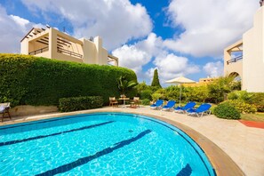 A swimming pool with lounge chairs and a table, surrounded by greenery and modern architecture. - Villa Vaso in Roussospiti (Rethymno)