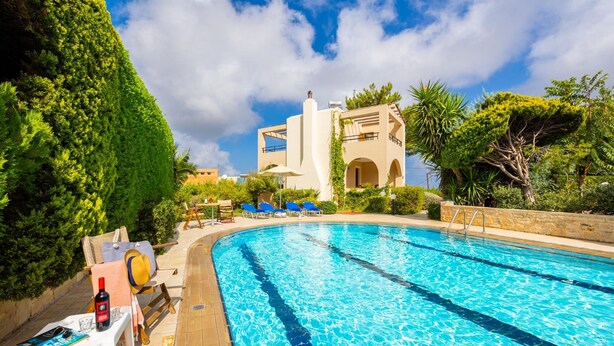 A swimming pool with clear blue water, surrounded by greenery and a building with a modern design. - Villa Vaso in Roussospiti (Rethymno)