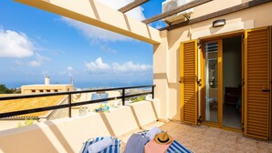 A balcony with two striped lounge chairs, a hat, and a towel, overlooking a cityscape and the sea. - Villa Vaso in Roussospiti (Rethymno)