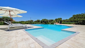 Ein rechteckiger Swimmingpool mit klarem, blauen Wasser, umgeben von einer gefliesten Terrasse.