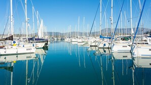A marina with numerous sailboats docked in calm waters, surrounded by hills.