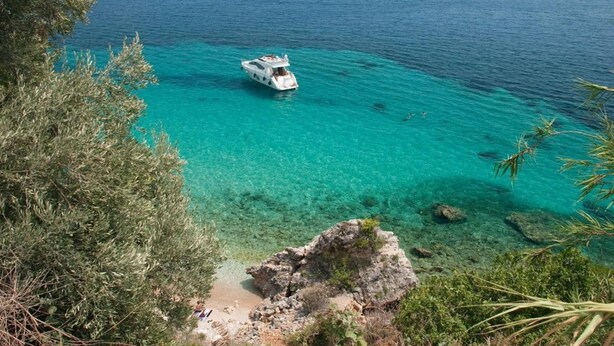 A boat on clear turquoise waters with rocky terrain and vegetation in the foreground.