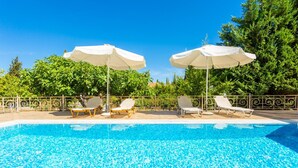 A swimming pool with clear blue water, surrounded by white umbrellas and lounge chairs.