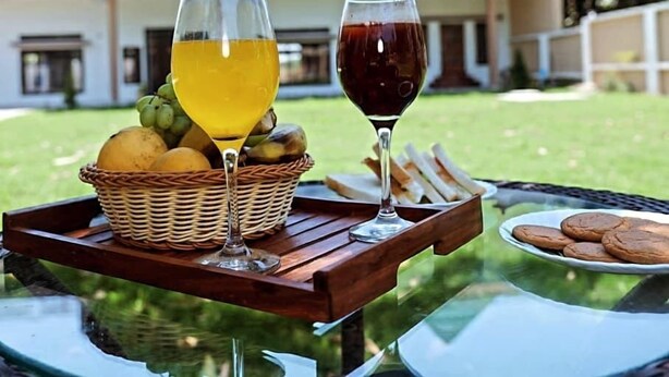 A table with a fruit basket, two glasses of beverages, and a plate of cookies. - Atithi Stays (Ramnagar)