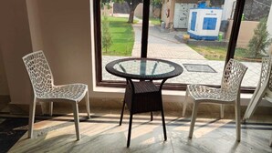 A room with two white wicker chairs and a glass table. - Atithi Stays (Ramnagar)