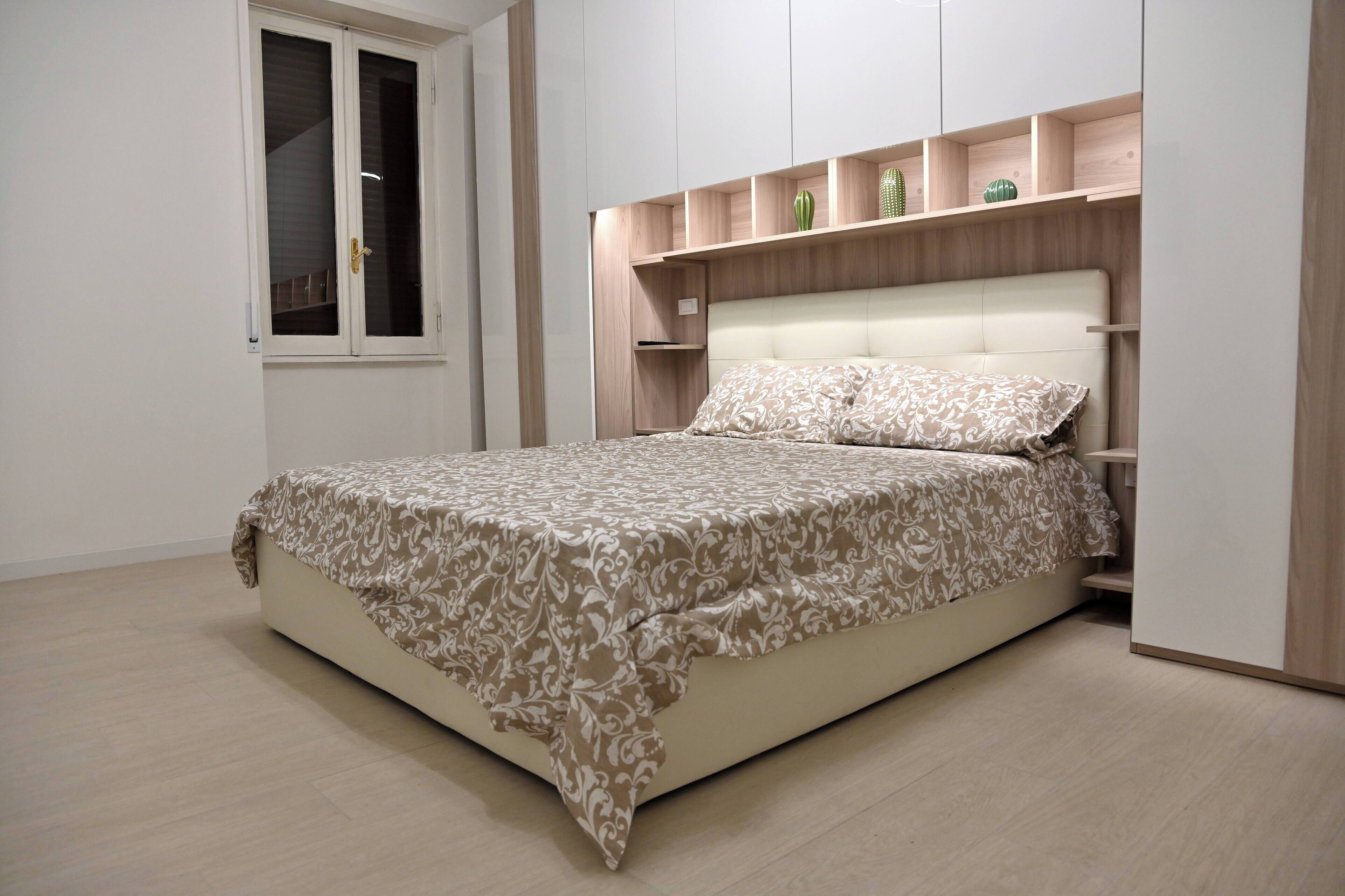 Camera da letto con un letto, una finestra e mensole integrate con oggetti decorativi.
