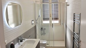 A modern bathroom with a large mirror, a sink, a toilet, and a shower. - Emerenziana Lovely Apartment (Rome)