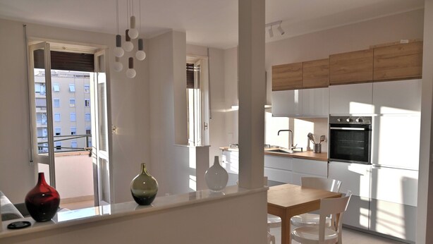 A modern kitchen with white cabinets, a wooden countertop, and a dining area with white chairs. - Emerenziana Lovely Apartment (Rome)