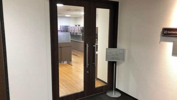 Een hotelingang met een glazen deur, een bord voor een restaurant, en een bord dat aangeeft dat het restaurant 24 uur per dag geopend is.