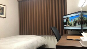 Een hotelkamer met een bed, een bureau met een computermonitor en een raam met bruine gordijnen.