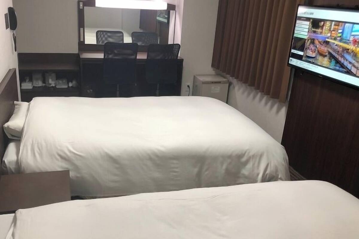 Une chambre d’hôtel avec deux lits, un bureau, une chaise, une télévision et un miroir.