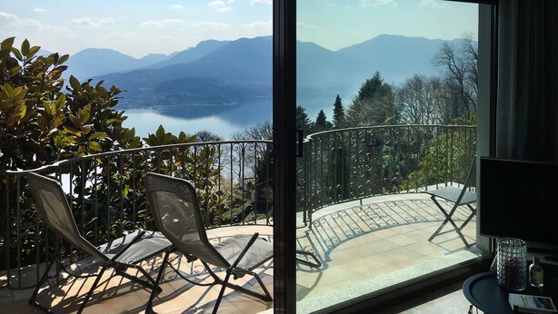 Un balcon avec vue sur les montagnes et un lac. On y trouve deux chaises et une table.