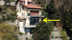 Une maison à deux étages, avec un toit recouvert de tuiles rouges, un balcon et une grande fenêtre.