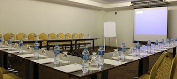Un salón de conferencias con una larga mesa, sillas, botellas de agua, una pizarra y una pantalla de proyector.