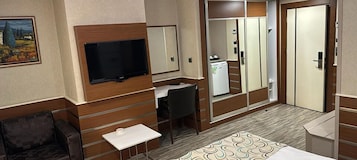 Una habitación de hotel con cama, escritorio, silla, televisor, armario y una mesita.