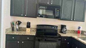 A kitchen with dark cabinets, a black stove, a microwave, and a coffee maker. - Book Now! Disney and Theme Parks Days, Poolside Family Villa Awaits! (Davenport)