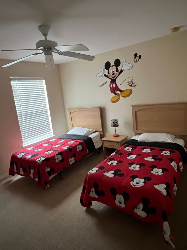 A hotel room with two beds, each with a Mickey Mouse themed bedspread, a ceiling fan, a window with blinds, and a wall decal of Mickey Mouse. - Luxurious 4-bedroom Apartment With Private Pool in Davenport (Davenport)