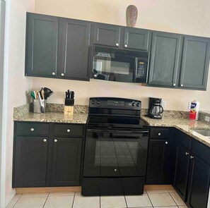 A kitchen with dark cabinets, a black stove, a microwave, and a coffee maker. - Luxurious 4-bedroom Apartment With Private Pool in Davenport (Davenport)