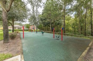 A playground with swings and climbing structures, surrounded by trees and a building in the background. - Luxurious 4-bedroom Apartment With Private Pool in Davenport (Davenport)