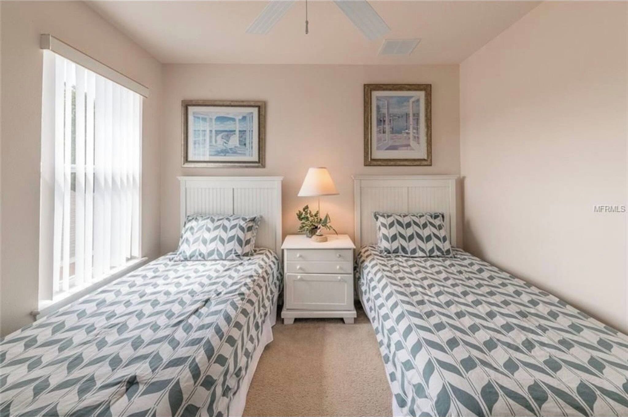 A bedroom with two beds, a nightstand with a lamp, and two framed pictures on the wall.