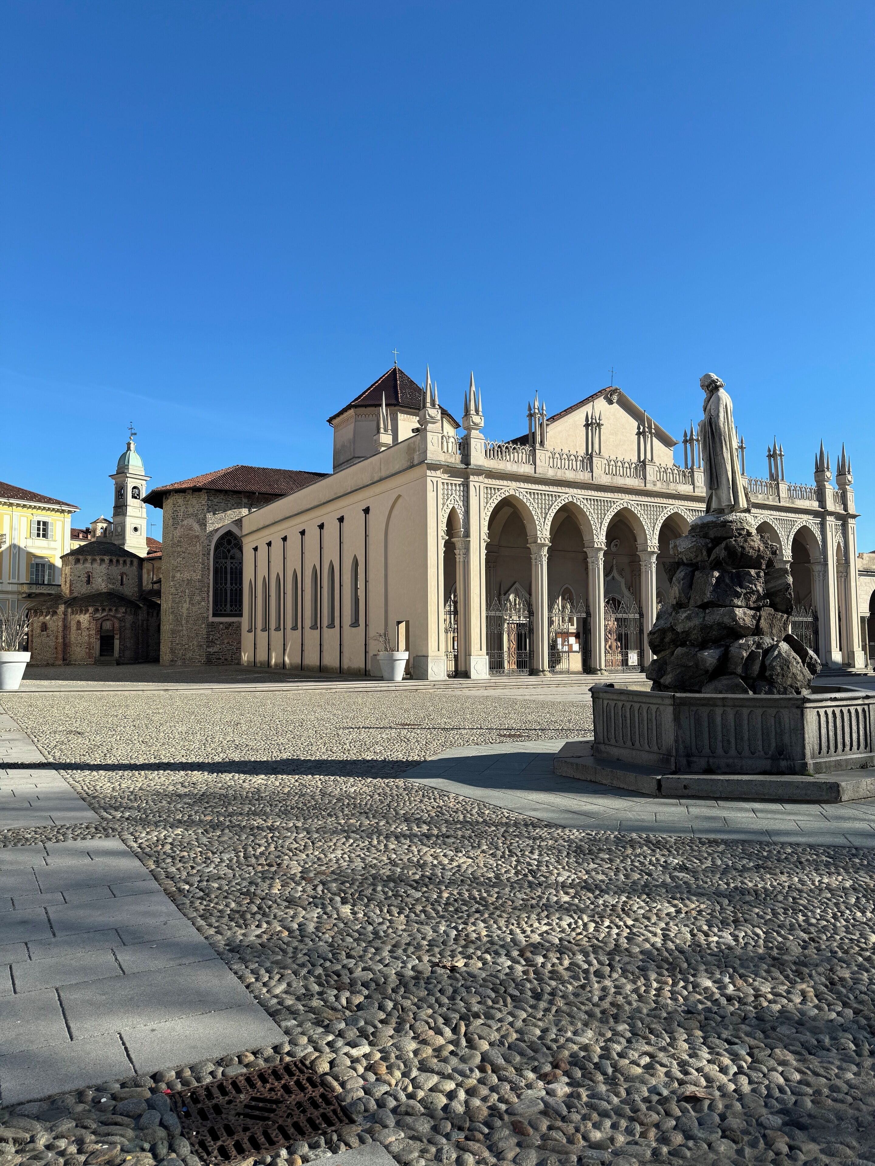 A historic building with a prominent statue in front, a clock tower, and a paved plaza with cobblestones.