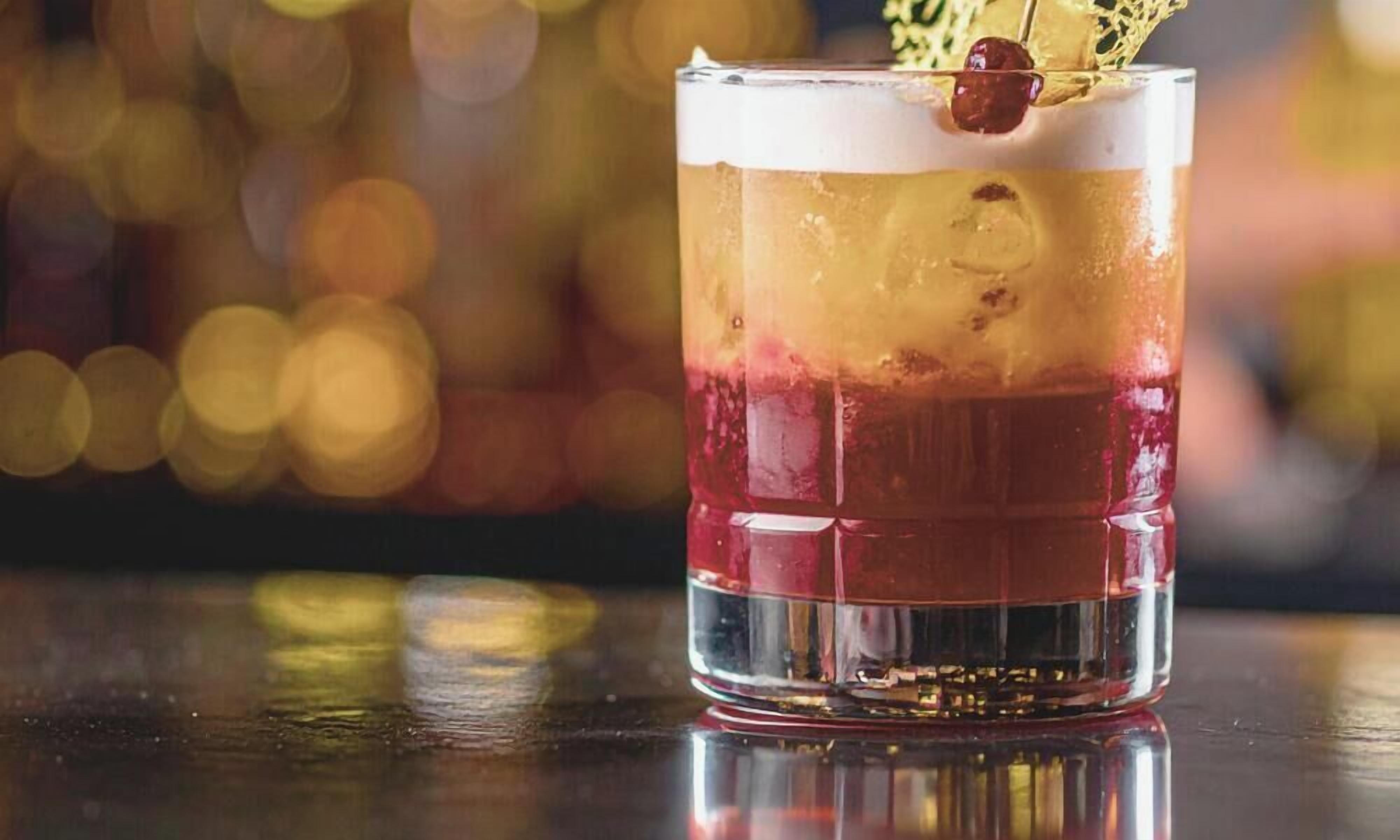 Ein mehrschichtiger Cocktail im Glas, mit einer Kirsche als Dekoration.