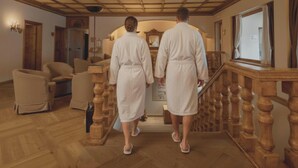 Vestíbulo de hotel con suelo de madera, una escalera con barandillas y un mostrador de recepción.