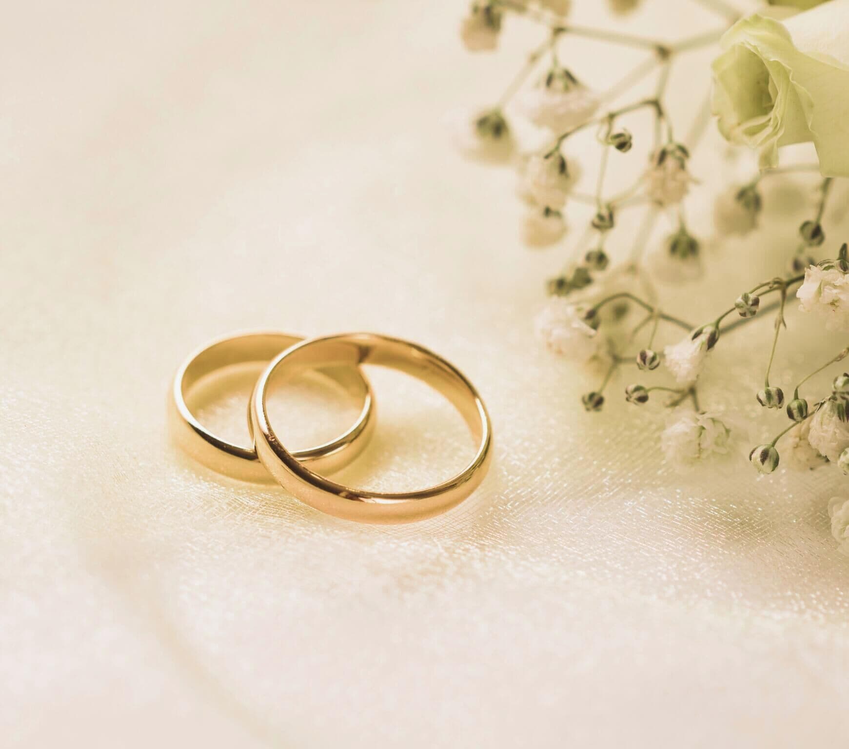 Two gold rings on a textured surface with white flowers.