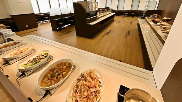 A buffet area with various dishes, a seating area with chairs, and a counter with a coffee machine. - Hotel Alpha-One Himeji-Minamiguchi (Himeji)