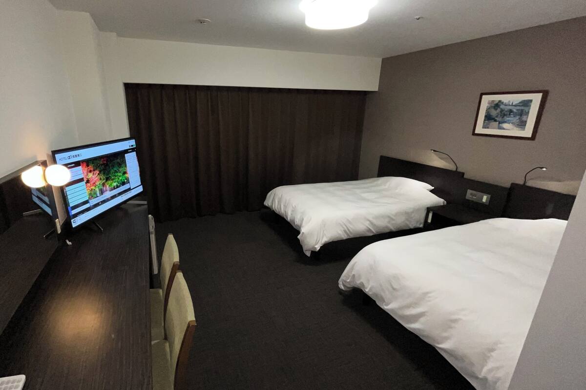 A hotel room with two beds, a TV on a stand, a desk with a phone, and a picture on the wall.