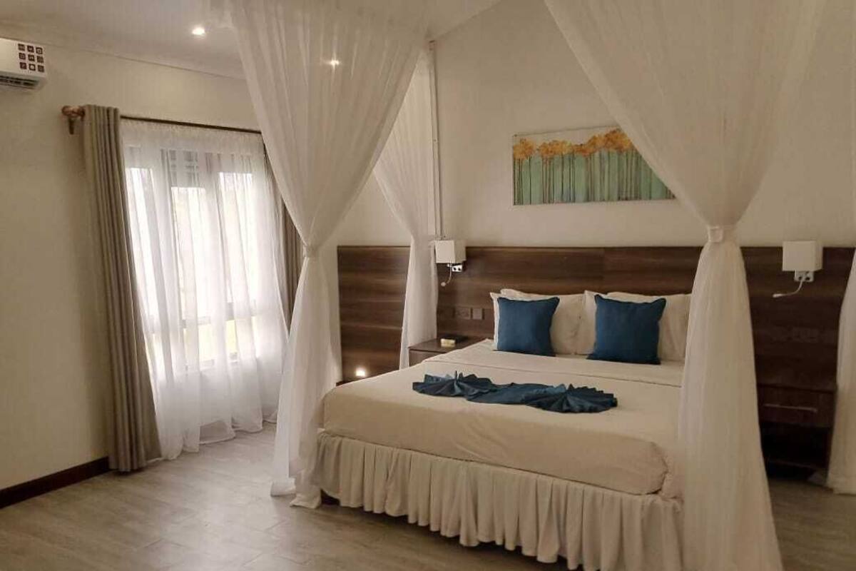 A bedroom with a large bed, white curtains, and a wooden headboard.