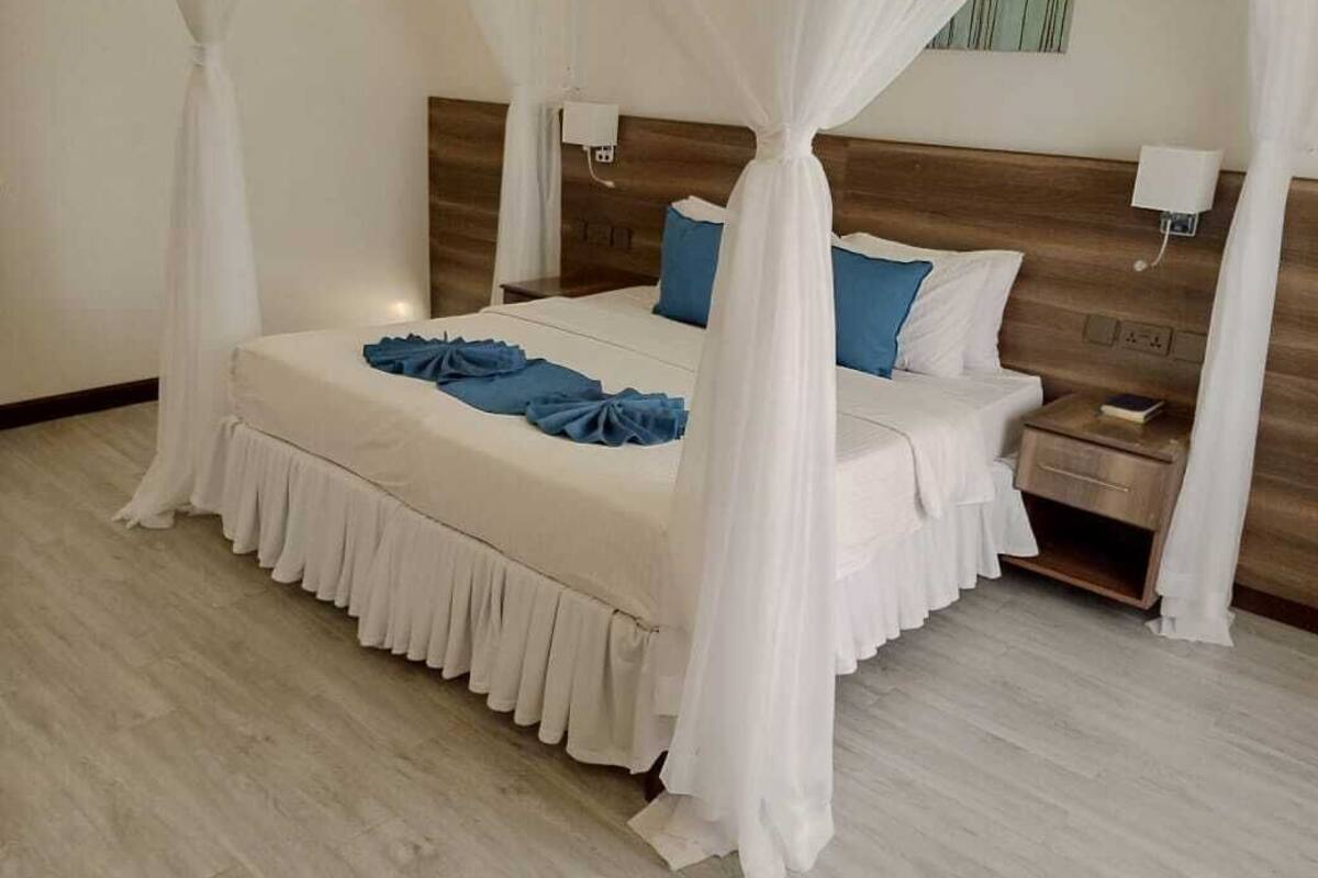 A bedroom with a bed covered in white bedding, a wooden headboard, bedside tables with lamps, and a nightstand.