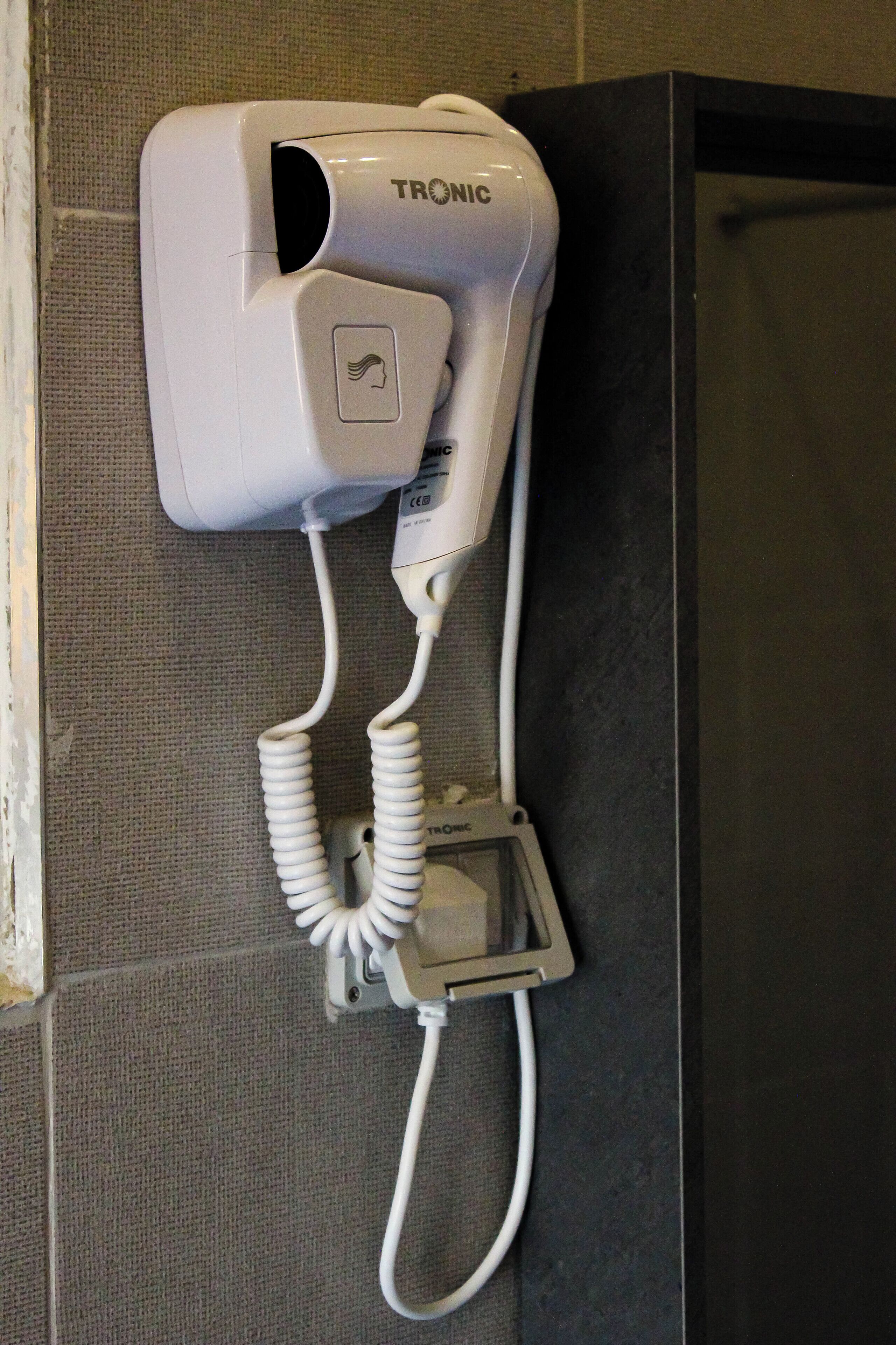 A TRONIC hair dryer mounted on a textured wall.
