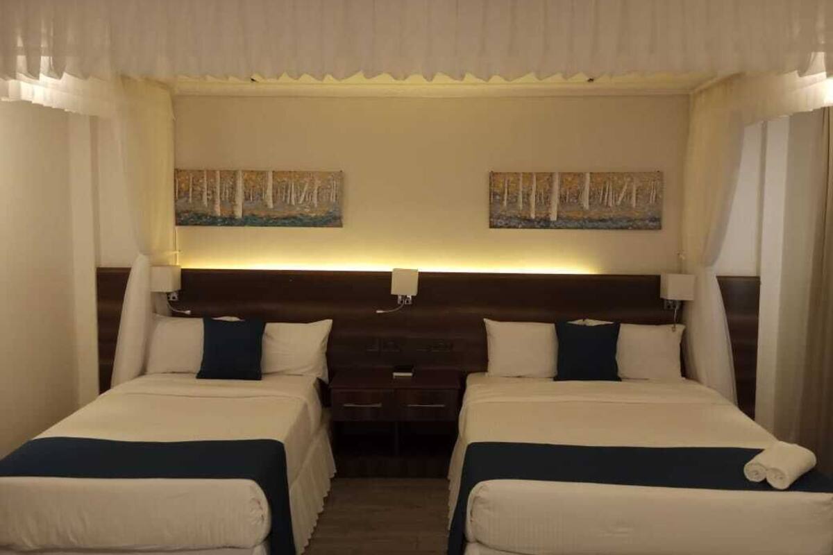 A hotel room with two beds, a wooden headboard, a nightstand, and two paintings on the wall.